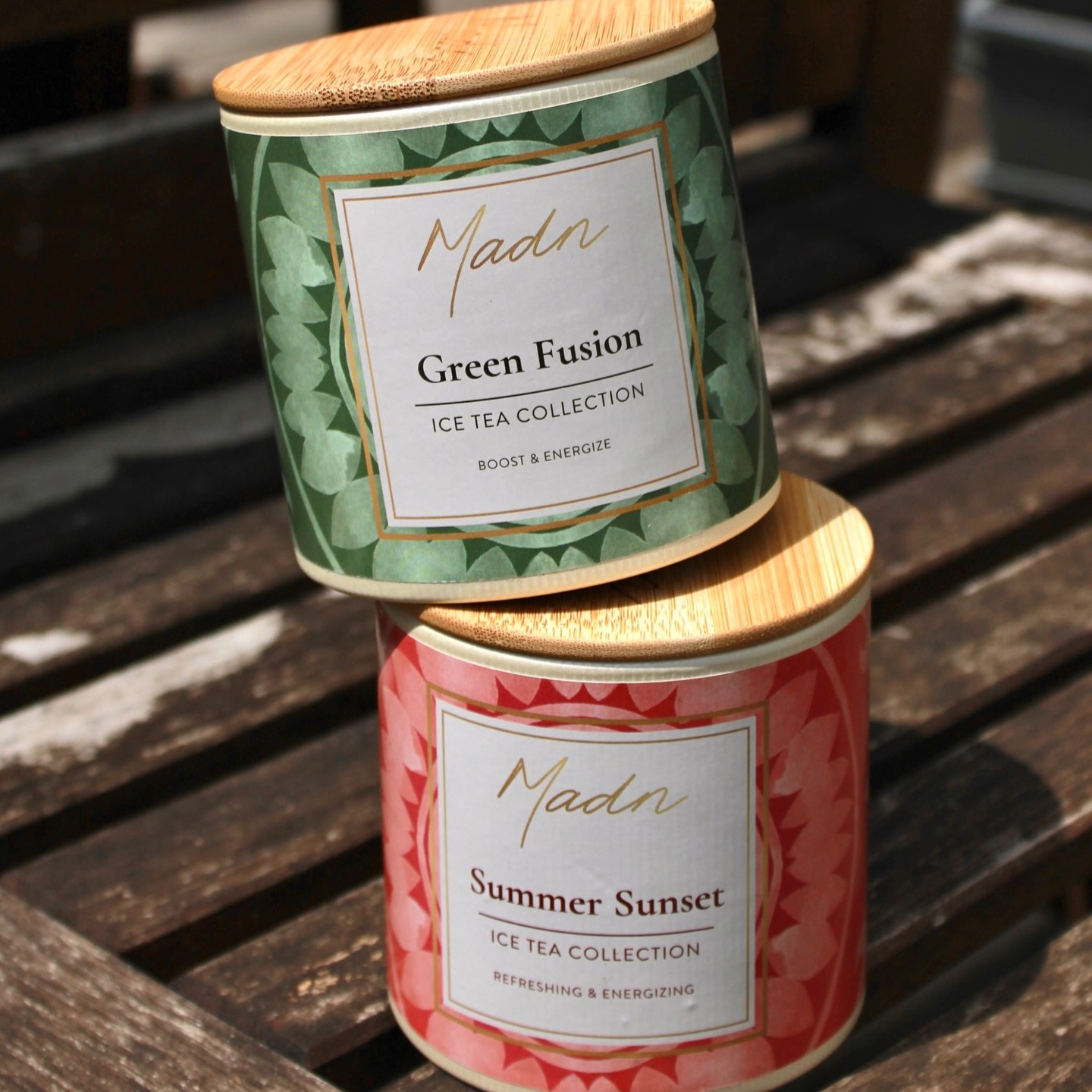 Madn Tea Ice Tea Collection — Green Fusion and Summer Sunset stacked bamboo-lid tins on a wooden table, labels reading “Boost & Energize” and “Refreshing & Energizing.
